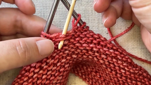 Hands knitting with red yarn.
