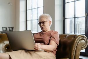 Senior lady sitting on a couch using a laptop.