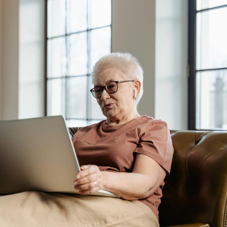 Senior lady sitting on a couch using a laptop.