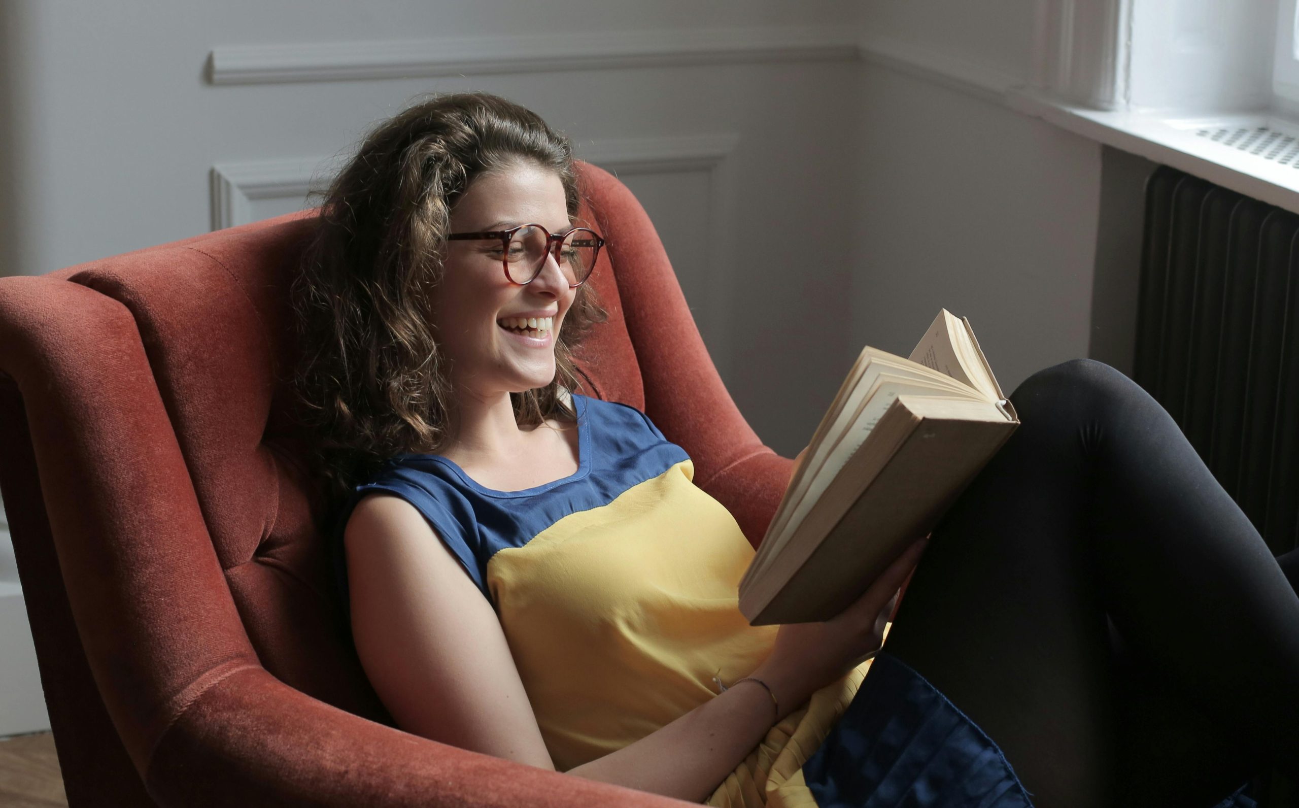 Young woman reading a book while sitting on an armchair at home.
